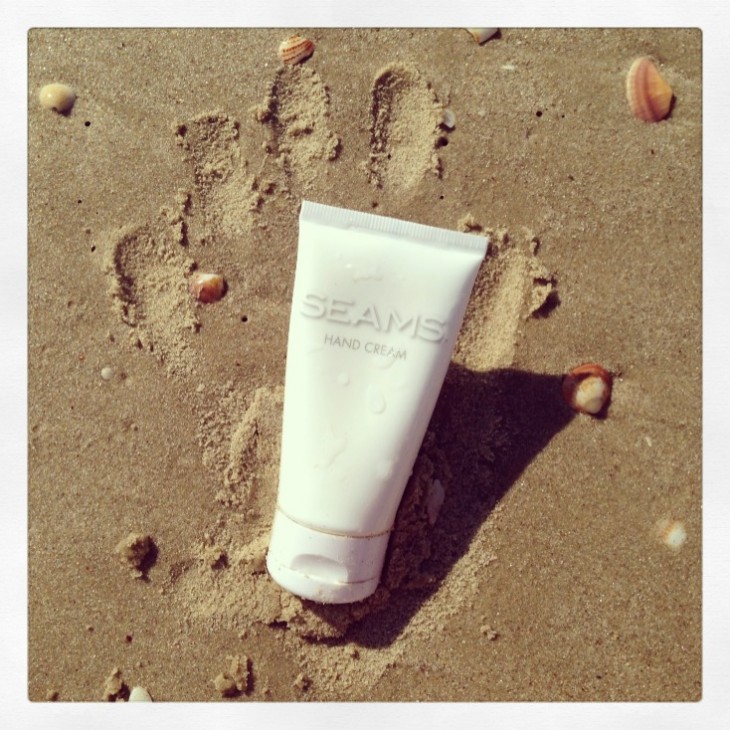 Image of Seams Hand Cream in the sand with handprint in the sand. Seams Hand cream image, seamsbeauty.co.uk